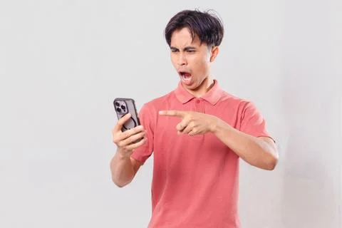 Young Asian man angrily using his mobile phone, isolated on plain backgroun.. Stock Photos
