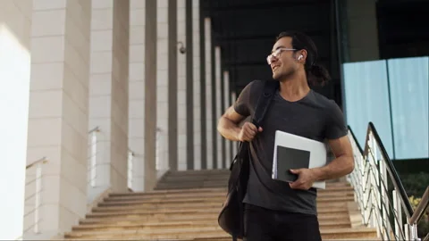 Young asian man with a backpack standing on the stairs, looking at the camera Stock Footage 253058887