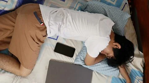 A young Asian man is in bed and asleep with his laptop 写真素材