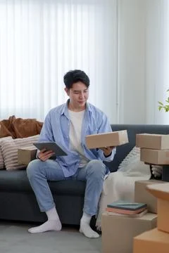 Young Asian man checking tablet and package while organizing online busines.. Stock-Fotos