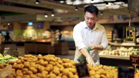 Young asian man chooses and picks in eco bag vegetables potato or fruits in the  Stock Footage 199845559