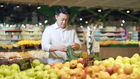 Young asian man chooses and picks in eco bag apple fruit or vegetables  Stock Footage 199850262