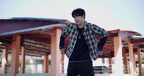 Young Asian man dances alone with full energy in an open-air public pavilion. 스톡 동영상 313178945