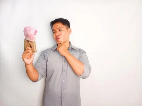 Young Asian man doing thinking gesture while holding Indonesia paper money Stock Photos