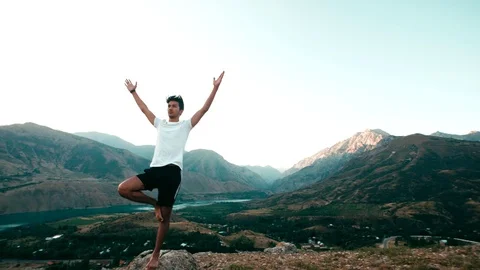 Young Asian man doing yoga in a mountain area, standing on top of a mountain Stock Footage