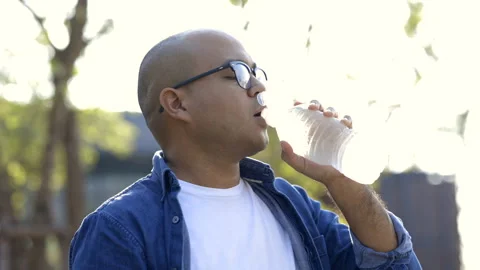 Young asian man drinking cool water from bottle of water in the park. Video stock 153446071