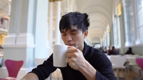 Young Asian Man Drinking Hot Cup of Coffee at Cafeteria in Morning Stock Footage 117969919