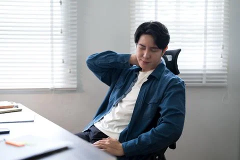 Young Asian man experiencing back pain and discomfort while working at mode.. Stock Photos