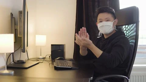 A young Asian man in a face mask looks at a desktop computer screen at home and Stock-Footage 138147953