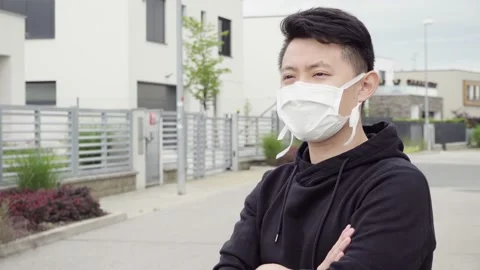 A young Asian man in a face mask looks around, thoughtful, in an empty suburban Stock Footage 138152001