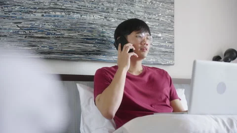 Young Asian Man Freelancer using Laptop and talking on cell phone. Video stock 213581316