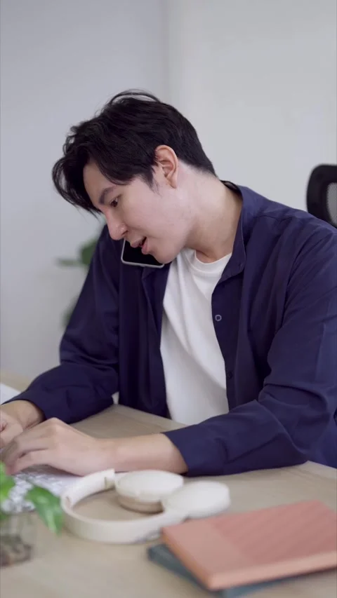 Young Asian man freelancer working remotely while talking on phone at home .. Stock Footage 337650536