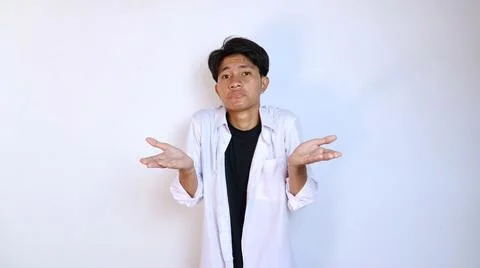 Young asian man gesturing not knowing how, confused by stretching out his t.. Stock Photos