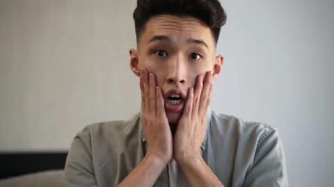 Young Asian man gets scared watching horror TV program Stock Footage 182370426