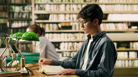 Young asian man with glasses reading book at library study table Stock Footage 336360885