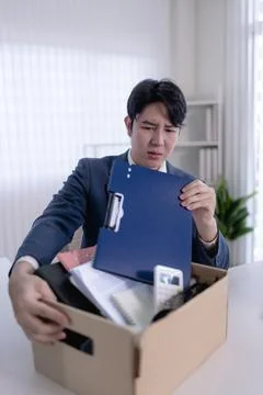 Young Asian man holding folder examining belongings in cardboard box after .. Foto stock