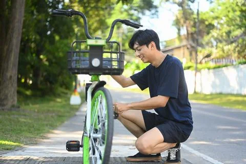 Young asian man inspecting a bicycle before riding in public park Stock Photos