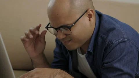 Young asian man lay down on sofa in living room and using laptop. He rubbing his Stock Footage 153011850