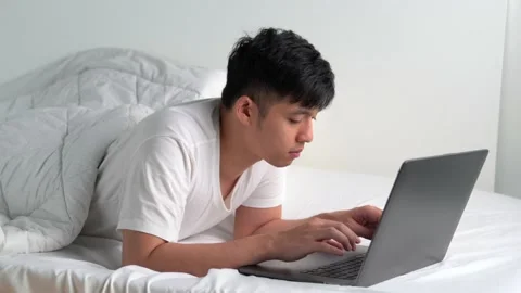 Young Asian man lying in the bed and using laptop Stock Footage 156639318