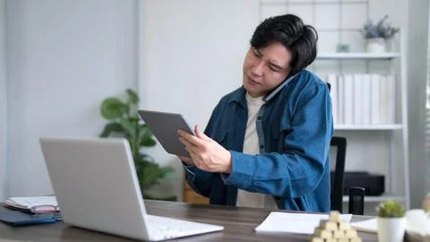Young Asian man multitasking with tablet and laptop while standing in moder.. Stock Photos