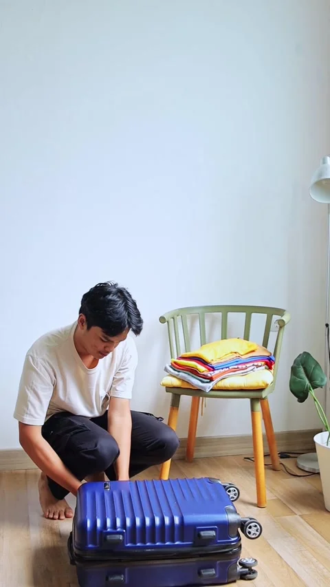 Young asian man opened packing blue suitcase preparing packing colorful clothes 動画素材 319644326