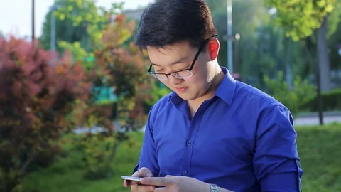 Young Asian man in a park talking on the phone. Stock Footage 90277723
