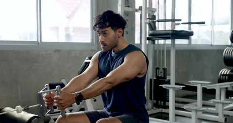 Young Asian man performs seated cable row in modern gym, pulling grip handle Stock Footage 337811350