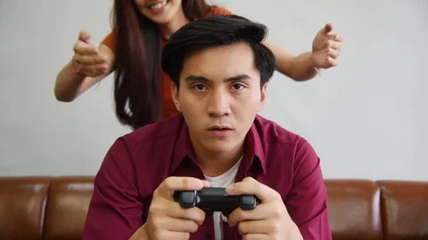 Young Asian man playing console game and get closed eyes by his girlfriend Stock Footage 121775629
