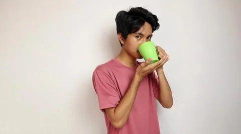Young asian man posing drinking from a cup on an isolated white background... 写真素材