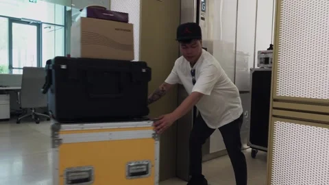 Young asian man pulling and rolling cases onto an elevator for an event Stock Footage 244787679