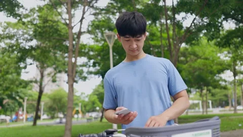 Young Asian man riding a shared bicycle with mobile phone after exercising Stock Footage 247038427