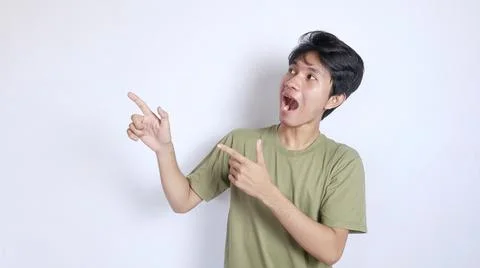 Young asian man shocked looking and pointing to the right side Fotos de archivo