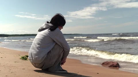 A young Asian man sits on the beach, gazing at the ocean waves Stock Footage 327132663