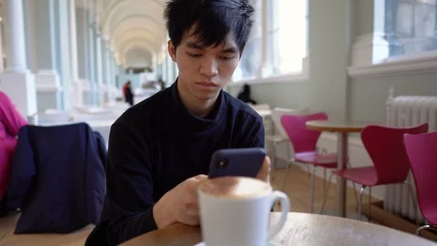 Young Asian Man Sitting at Cafe and Texting on Smartphone Stock Footage 117967151