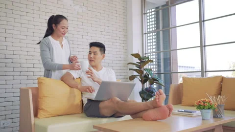 Young asian man sitting on the couch work with laptop while woman take a cup Video stock 147368448