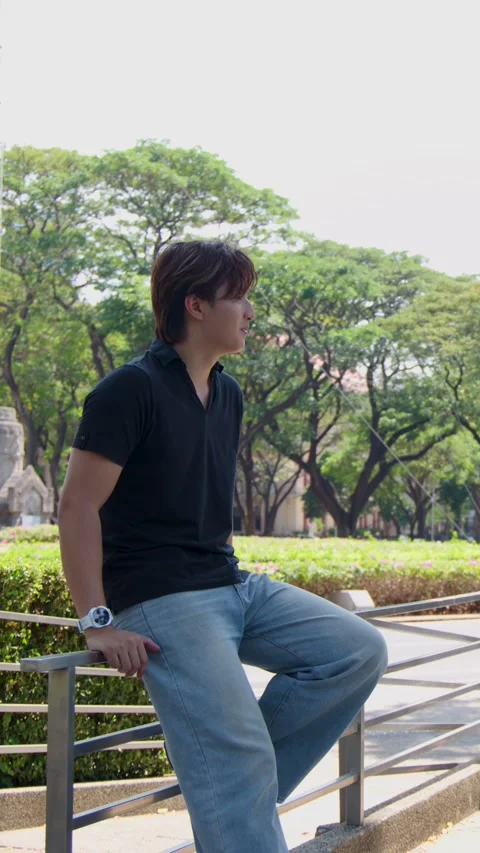 Young Asian Man Sitting on Railing at University Campus Park Stock Footage 338155565