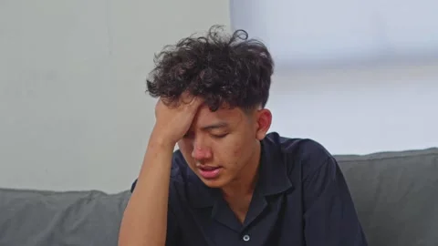 Young Asian man sitting on sofa shaking head suffering from severe vertigo Stock Footage 335909014