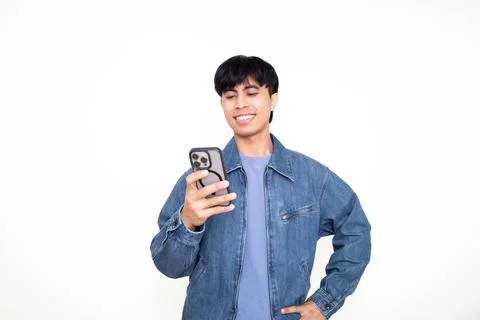 Young Asian man smiling while looking at his smartphone in a bright studio,.. Stock Photos