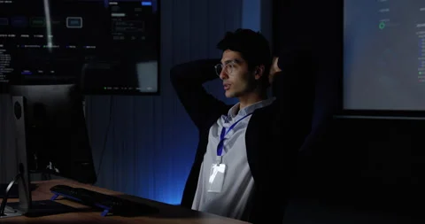 Young Asian man stretches at computer workstation, covers face and adjusts Stock Footage 343731229