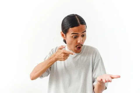 A young Asian man with a surprised expression pointing at his open palm iso.. Stock Photos