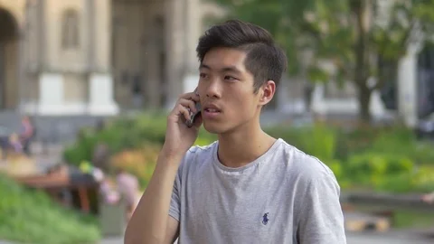 Young Asian Man talking on the phone in a park Stock Footage