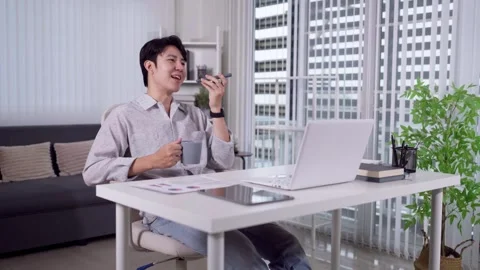 Young Asian man talking on phone holding coffee mug at home office desk wit.. Stock Footage 345156531