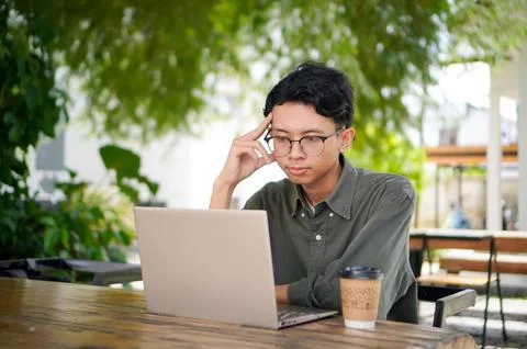 Young Asian man thinking while looking to his laptop. Stock Photos