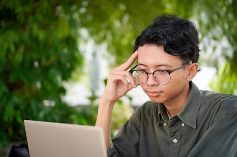 Young Asian man thinking while looking to his laptop. Stock Photos