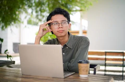 Young Asian man thinking while looking to his laptop. Stock Photos