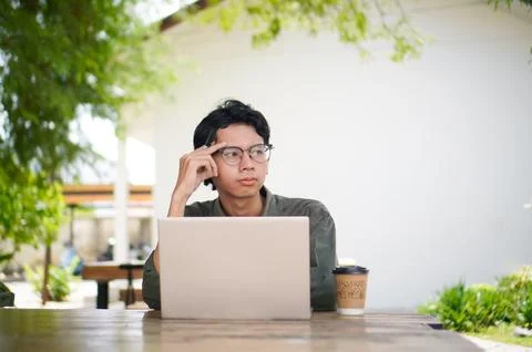Young Asian man thinking while looking to his laptop. Stock Photos