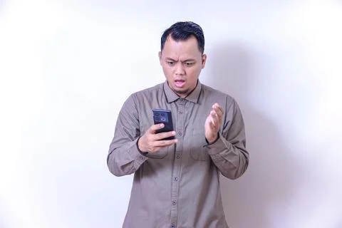 Young asian man thinking while looking at his smartphone with a puzzled exp.. Stock Photos