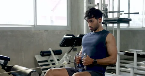 Young Asian man trains alone on seated cable row machine in modern gym, pulling Stock Footage 340072633