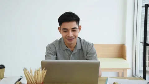 Young Asian man using laptop to working from home with happy and smile on face Stock Footage 144087443