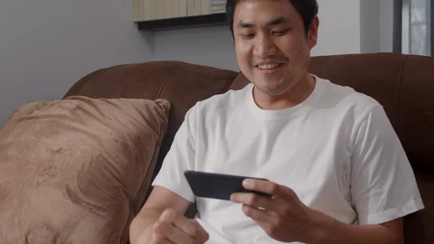 Young Asian man using mobile phone playing video games in television at home. Stock Footage 113572893